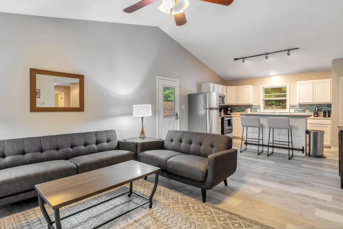 This inviting interior showcases a modern open-concept living space, featuring a stylish sofa and coffee table seamlessly connected to a sleek kitchen island. Warm lighting and cozy furnishings create an ideal atmosphere for relaxing, sharing meals, and spending quality time with family or friends.