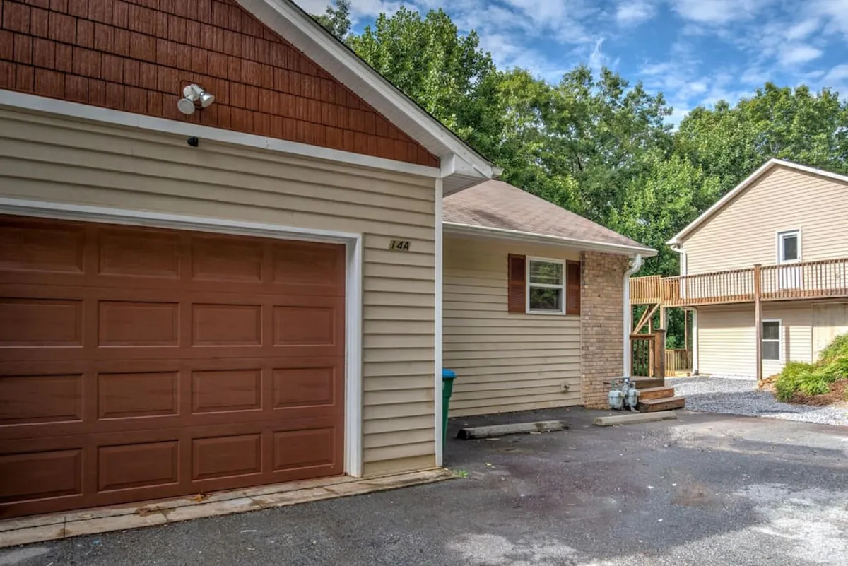 A view of the home's exterior featuring a garage door, side entrance, and landscaped surroundings. The driveway offers space for multiple vehicles, and the welcoming vibe is enhanced by well-kept greenery and glimpses of neighboring homes.