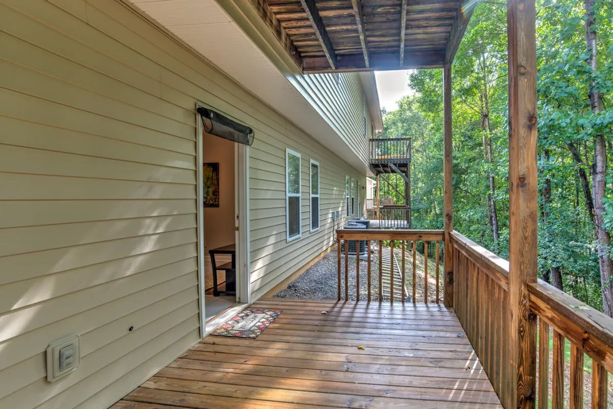 This image showcases an inviting wooden deck with an open door leading inside, surrounded by dense trees. The scene suggests easy indoor-outdoor flow, making it perfect for quick outings with pets or enjoying morning coffee while your pet lounges safely nearby.