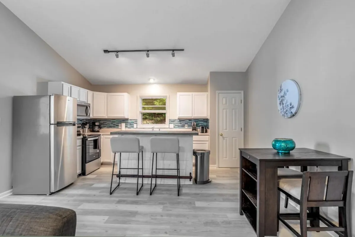 A sleek kitchen scene featuring a spacious island with bar stools, stainless steel appliances, and decorative wall art. The kitchen exudes a modern, welcoming vibe, with ample space for meal prep, casual dining, and social interaction.
