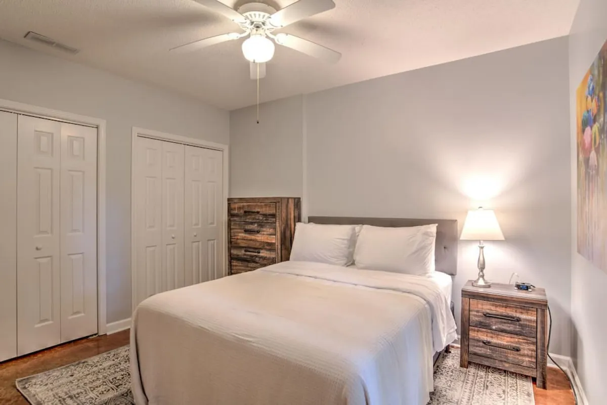 A tranquil bedroom featuring a king-sized bed with crisp white bedding, a stylish nightstand topped with a lamp, and vibrant, colorful artwork adorning the wall. Gentle natural light pours in, creating a serene and inviting atmosphere ideal for rest and relaxation.