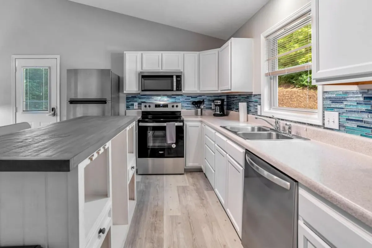 A spacious kitchen with a prominent kitchen island, modern stainless steel appliances, and a striking blue backsplash. The setup includes ample counter space and an inviting atmosphere, perfect for cooking and entertaining. The island serves as a central gathering spot, and the overall design is contemporary and functional.