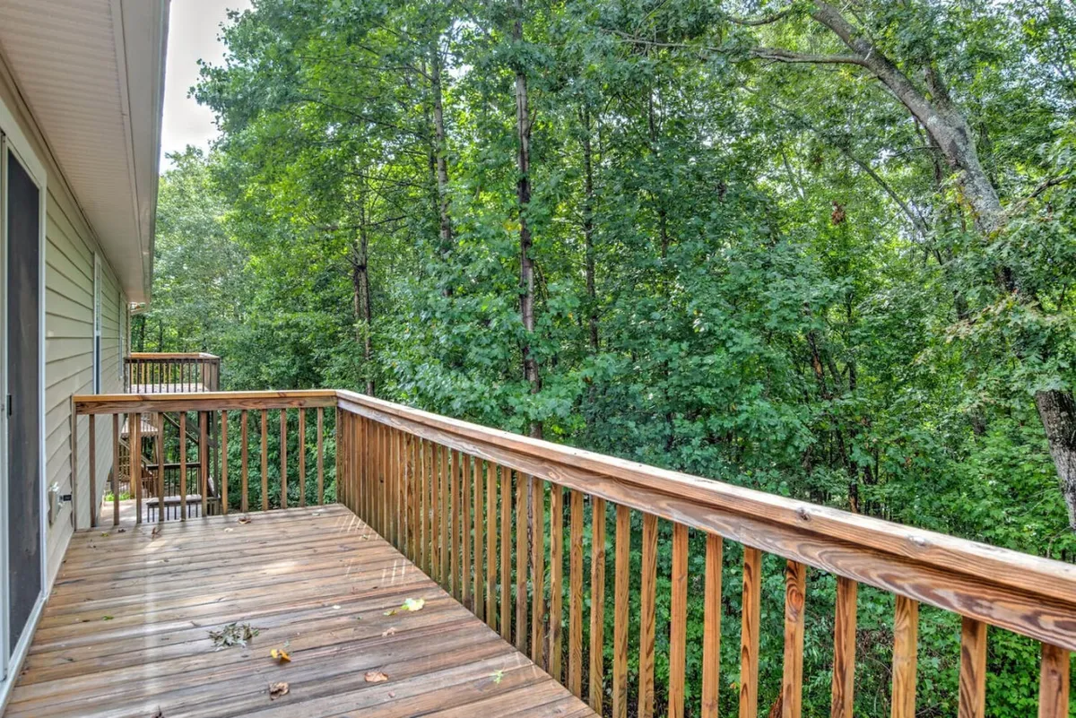 A spacious wooden deck surrounded by lush greenery, with sturdy railings and dappled sunlight filtering through mature trees. The scene captures a tranquil outdoor environment ideal for unwinding, reading, or observing wildlife, with a soft glow hinting at either early morning or sunset.